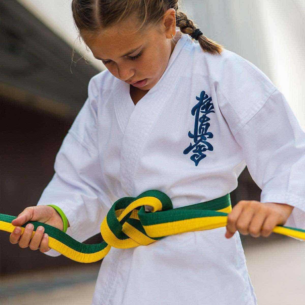 Girl tying a green and yellow FUJIMAE Kyokushinkai karate belt on white gi uniform