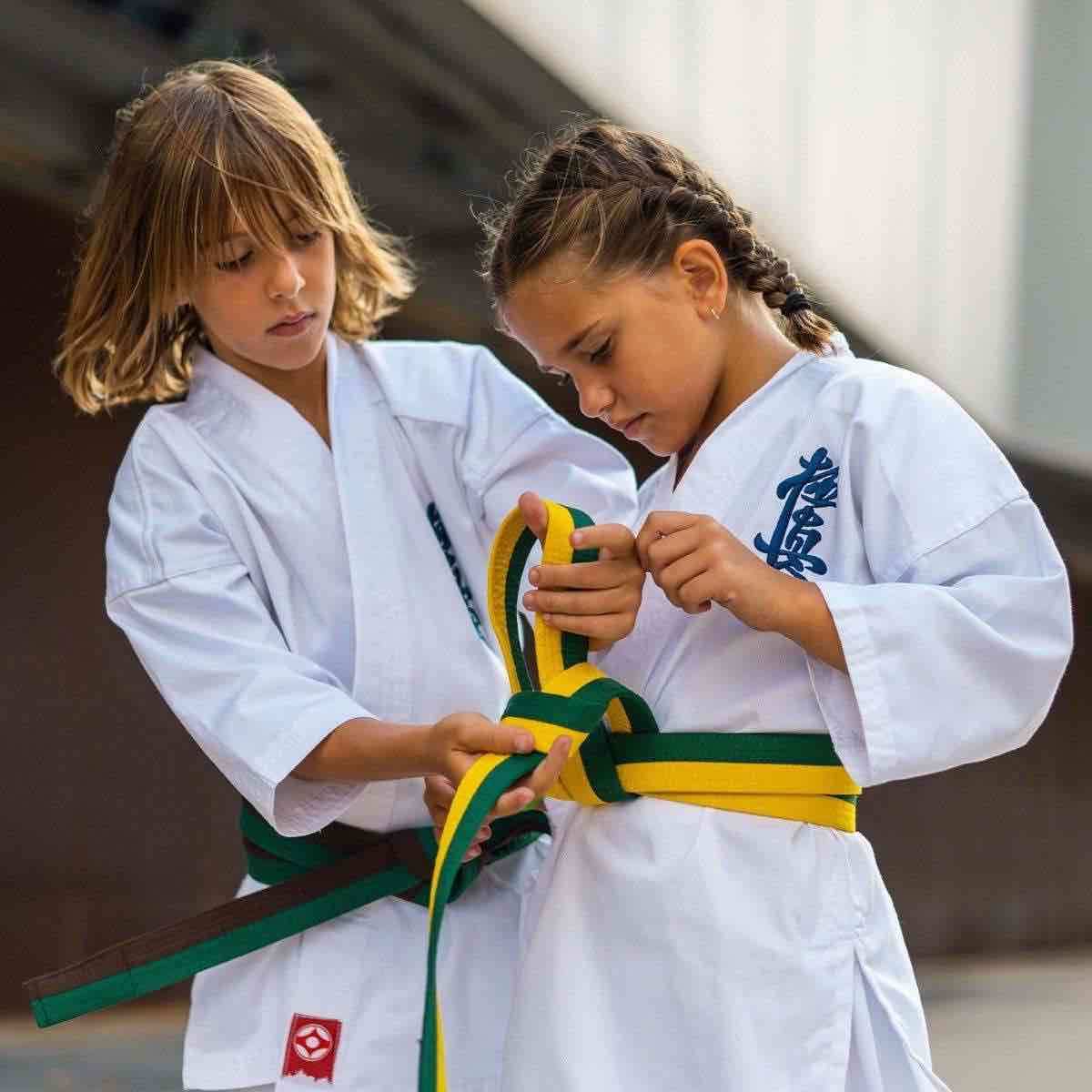 Two children in karate uniforms practicing with a Ceinture FUJIMAE Kyokushinkai bicolore belt in green and yellow during training