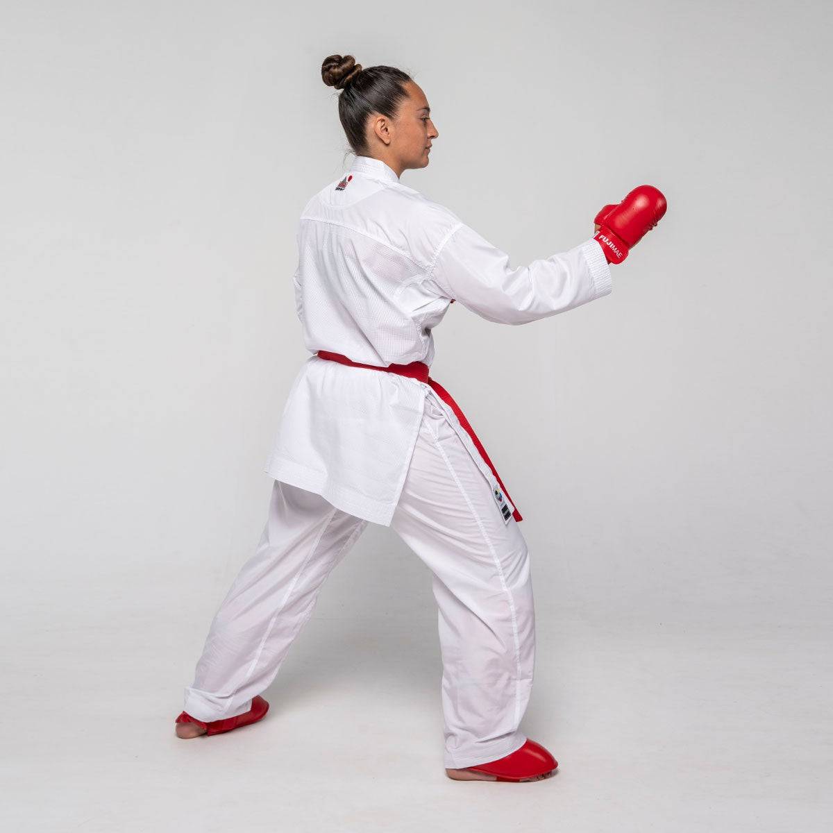 Professional karatéka wearing white lightweight FUJIMAE Kumite ProWear Hyperlite WKF-approved kimono with red belt and gloves in fighting stance