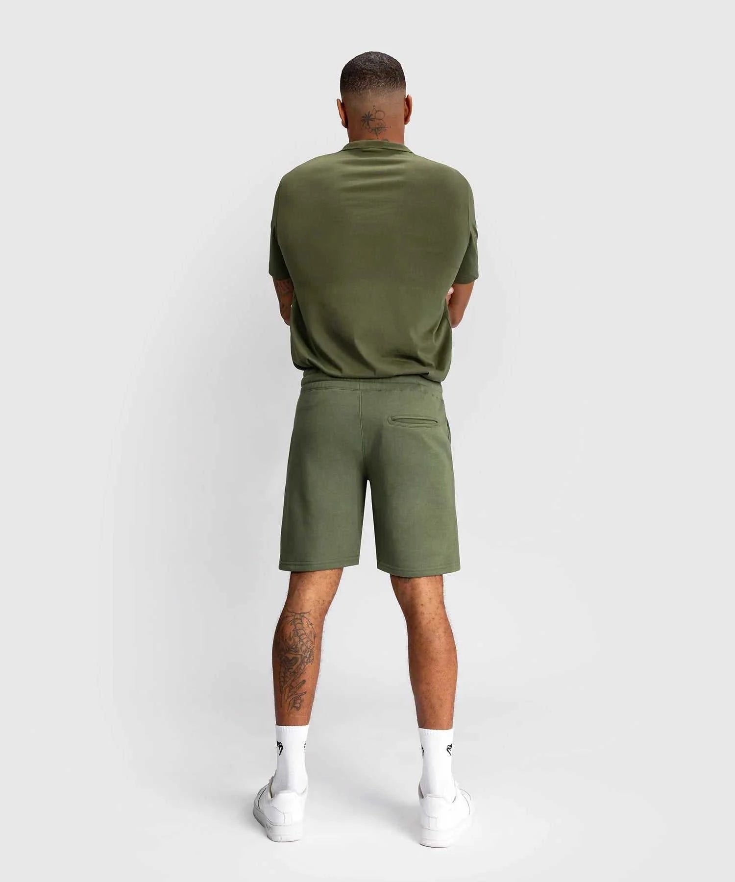 Back view of a man wearing kaki Shorts Venum Classic with matching t-shirt and white sneakers against a plain background